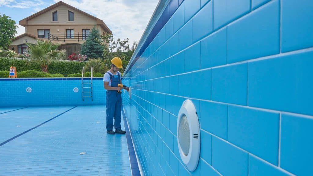 A Man is Working on the Side of a Swimming Pool — Taree Pool Supplies in Taree, NSW