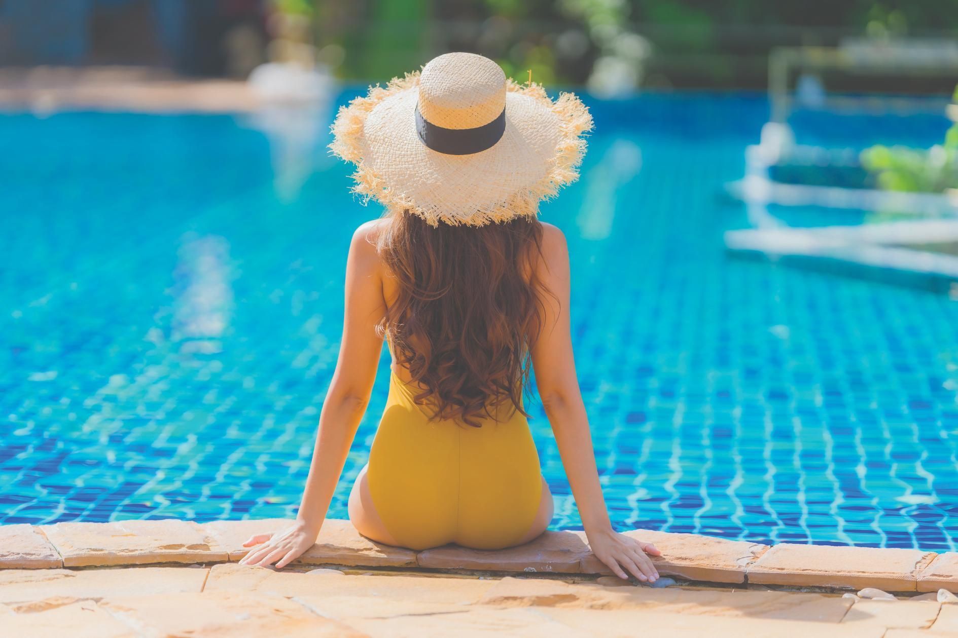 A Woman in a Yellow Swimsuit and Straw Hat is Sitting on the Edge of a Swimming Pool — Taree Pool Supplies in Taree, NSW