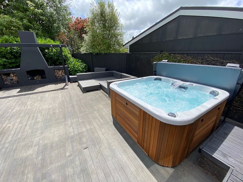 A Hot Tub is Sitting on a Wooden Deck Next to a House — Taree Pool Supplies in Taree, NSW