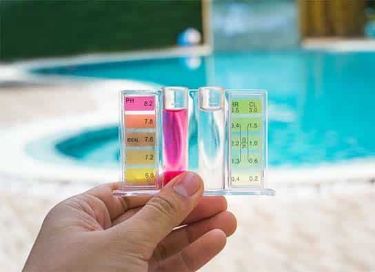 A Person is Holding a Test Tube in Front of a Swimming Pool — Taree Pool Supplies in Harrington, NSW