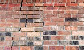 A person wearing work gloves places a red brick onto a wall under construction in front of a house.