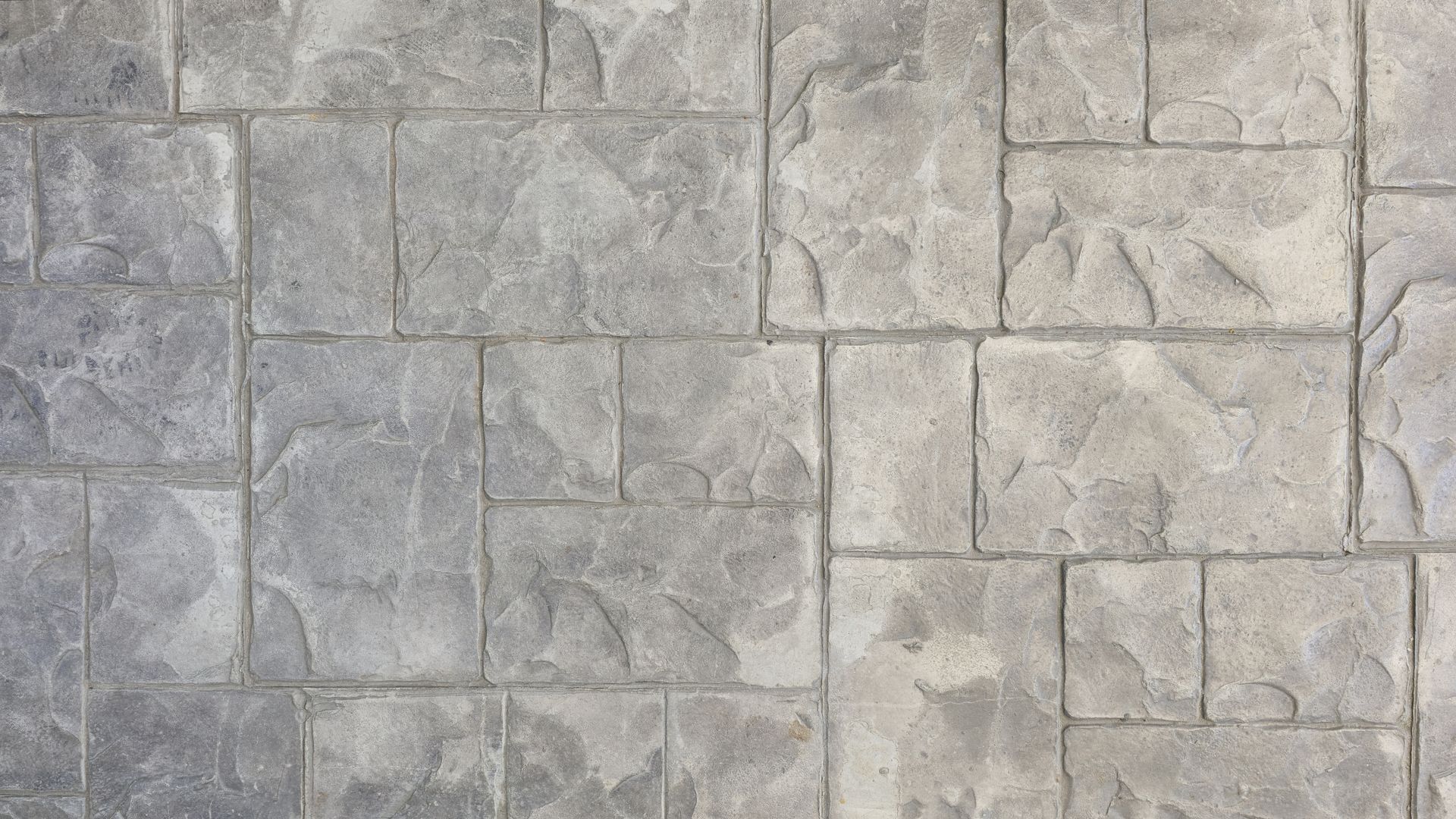 A close-up view of gray, textured concrete paving stones with a grid pattern of rectangular and square tiles.