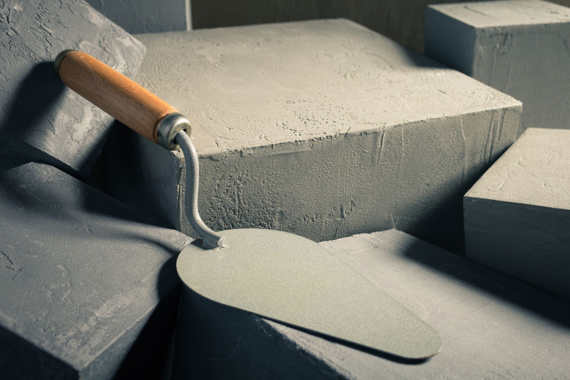 A metal masonry trowel with a wooden handle rests on stacked, gray concrete blocks.