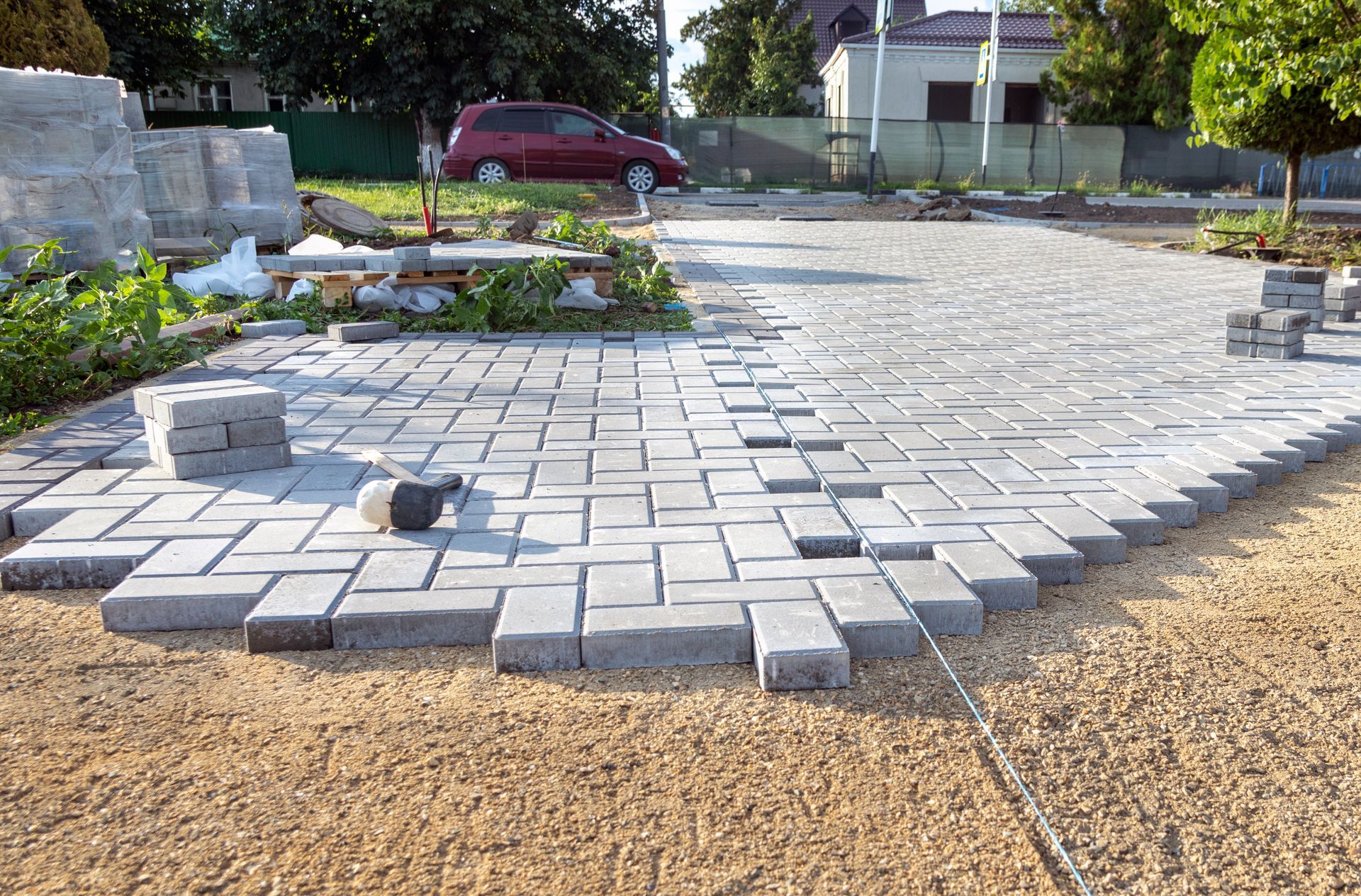 Grey paving stones arranged in a herringbone pattern on a gravel base during a patio construction project.