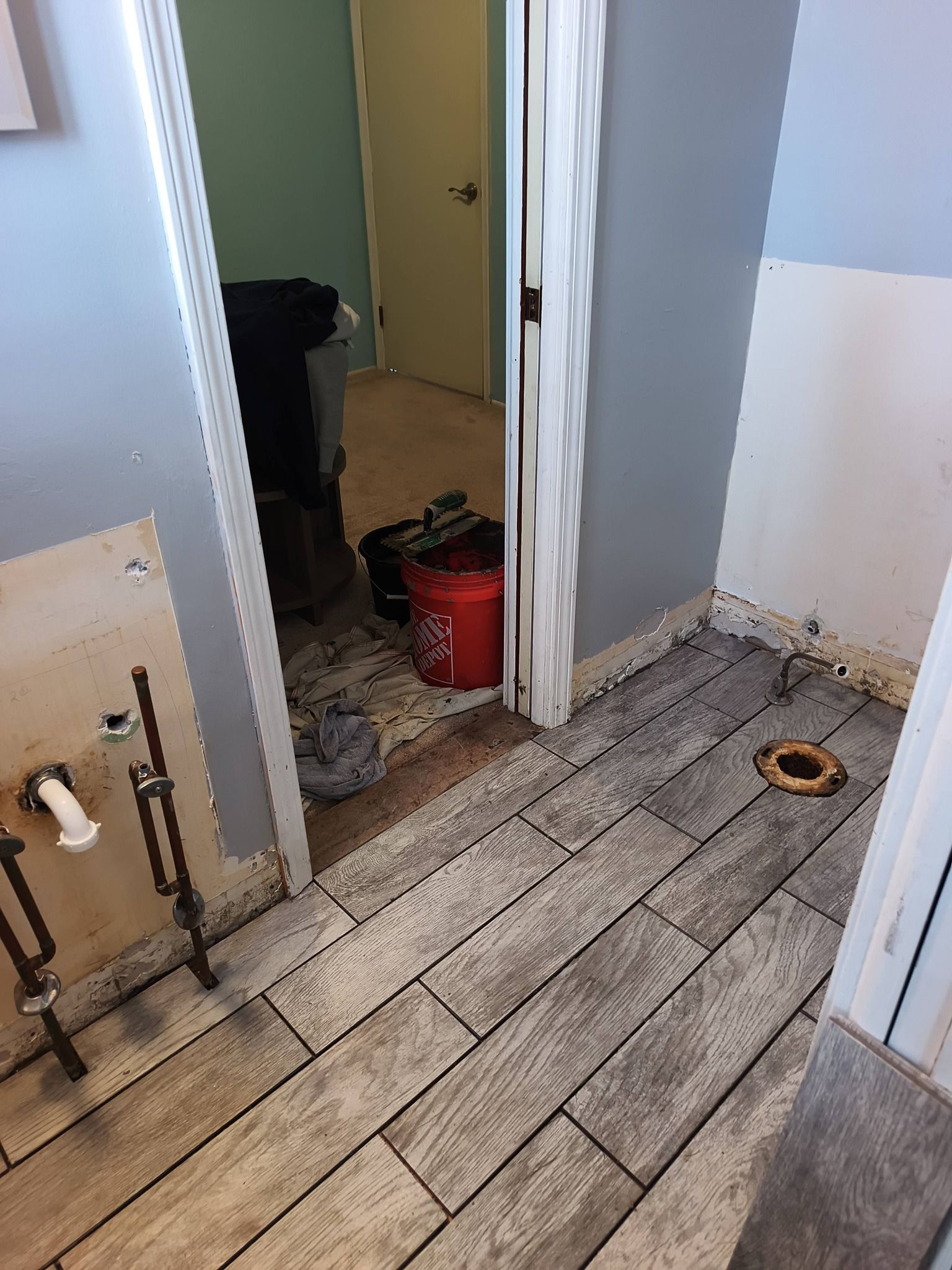 A bathroom undergoing renovation with unfinished walls, exposed plumbing, a toilet flange, and new wood-look tile flooring.