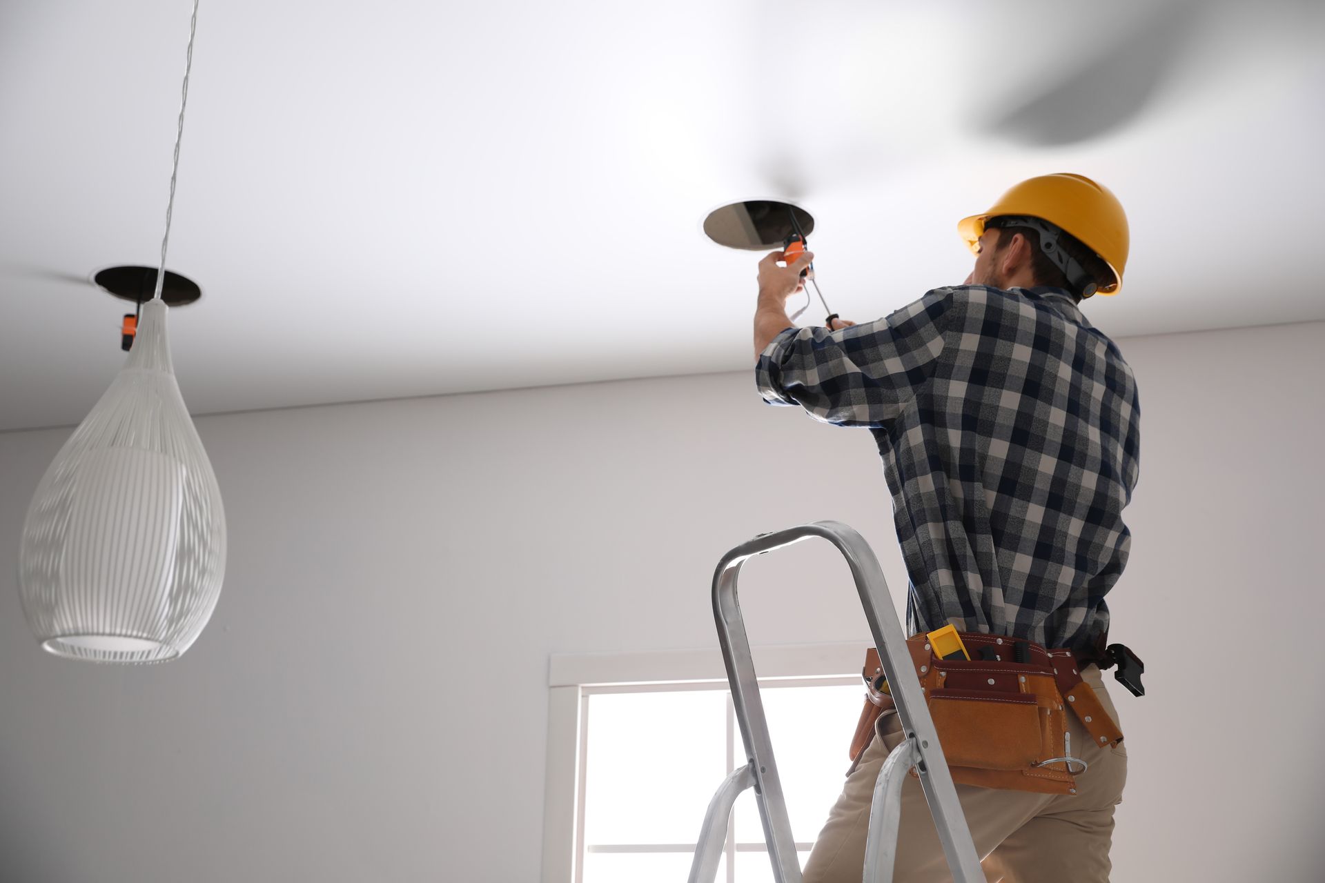 A man is standing on a ladder working on a ceiling.