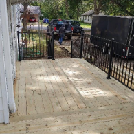 A newly built wooden deck with black metal railings, overlooking a driveway with a truck and trailer in the background.