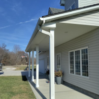 A front porch with white columns, light beige siding, and a white gutter system on a sunny day.