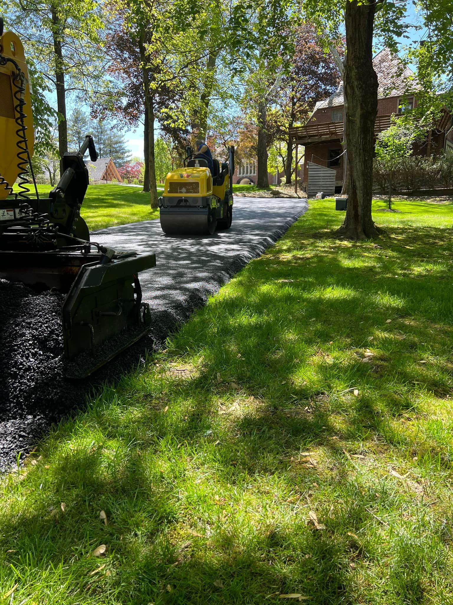 A machine is rolling asphalt on a driveway in a park.