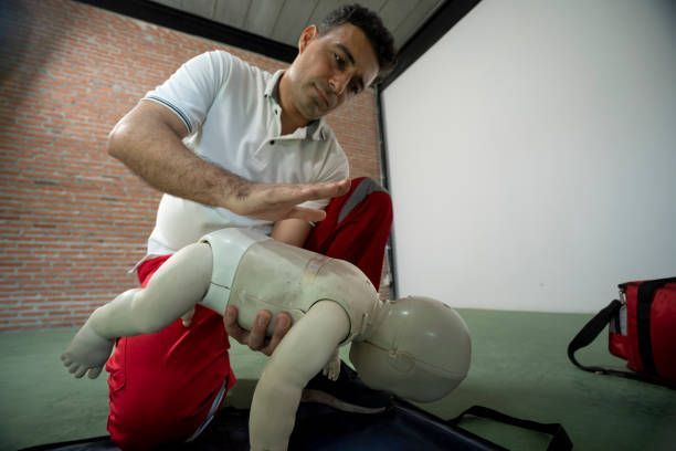 A man is kneeling down next to a baby mannequin.