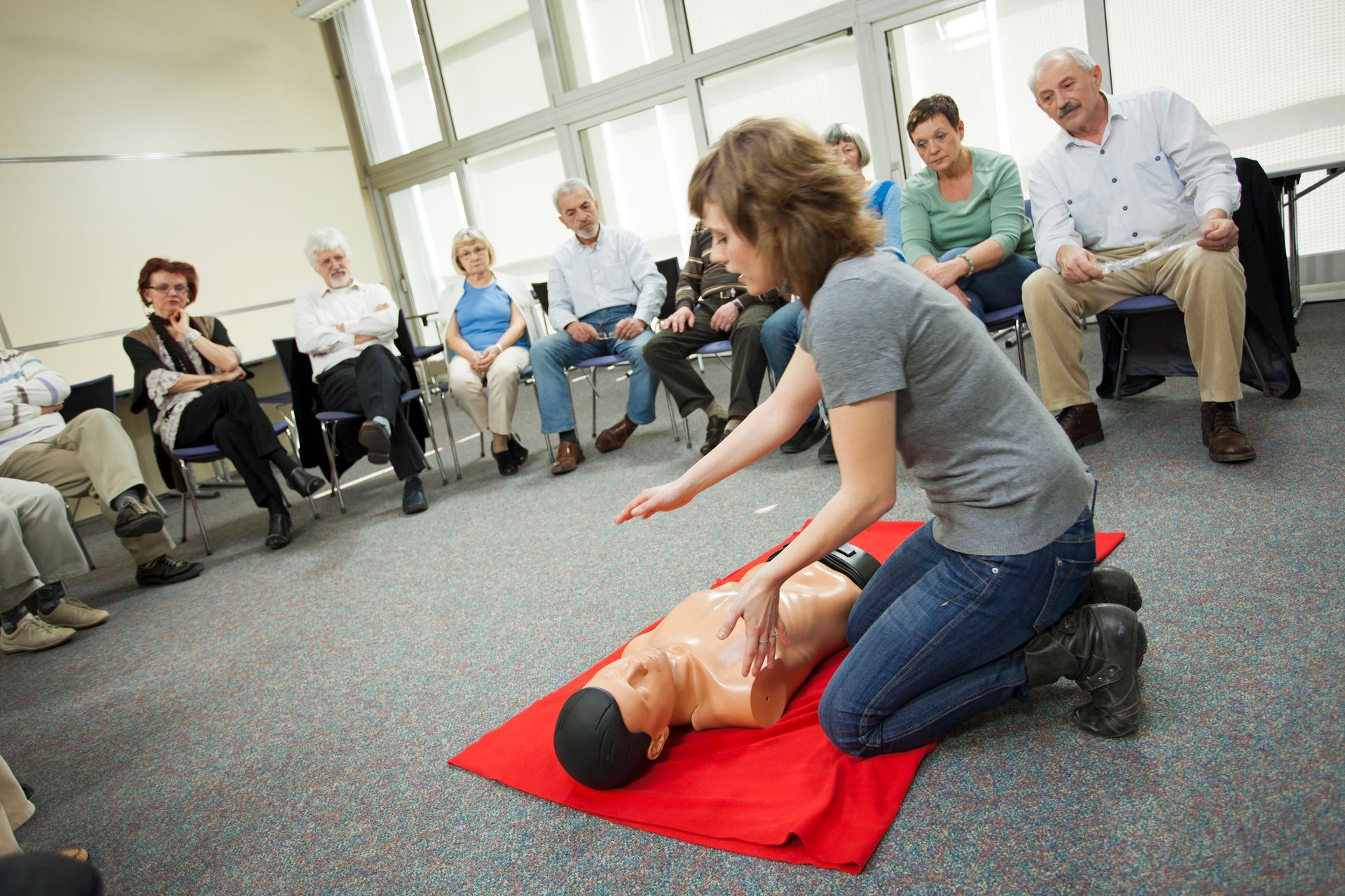 A woman is kneeling over a mannequin while a group of people watch.