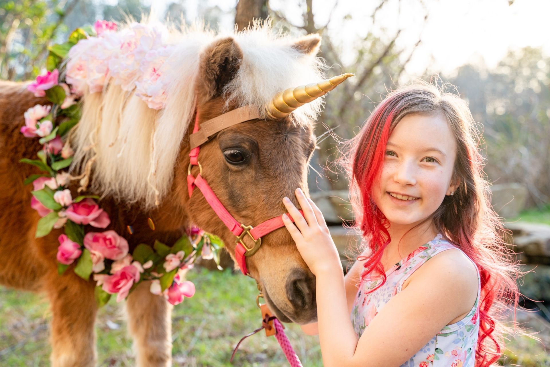 A little girl with red hair is petting a pony with a unicorn horn.