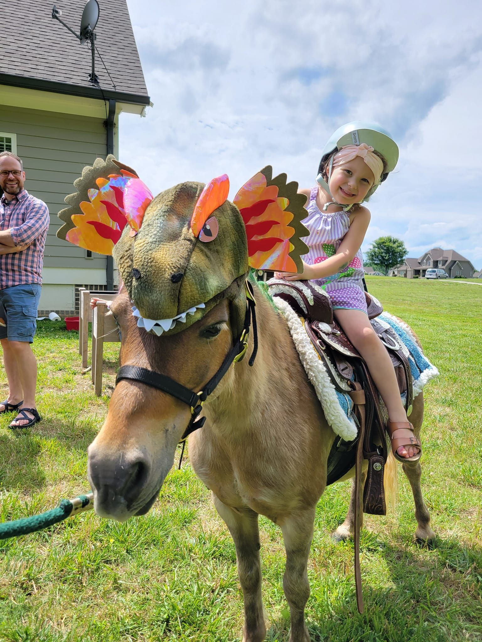 A little girl is riding on the back of a horse wearing a dinosaur costume.