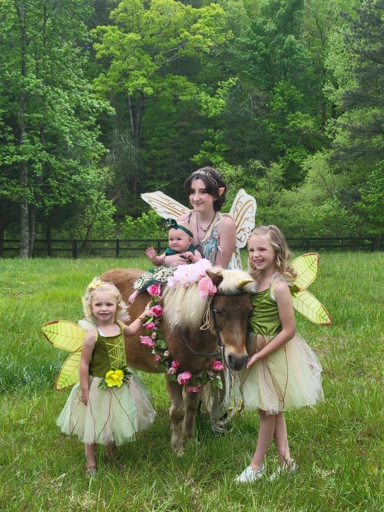 A woman and three little girls dressed as fairies are standing next to a pony.