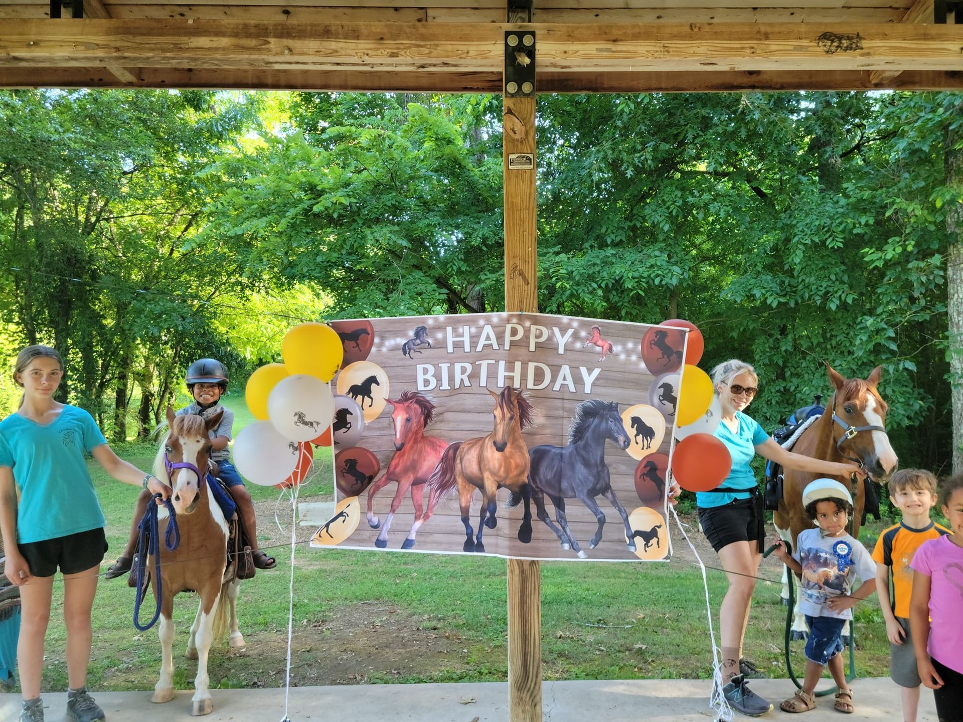A group of children are riding horses in front of a happy birthday sign.