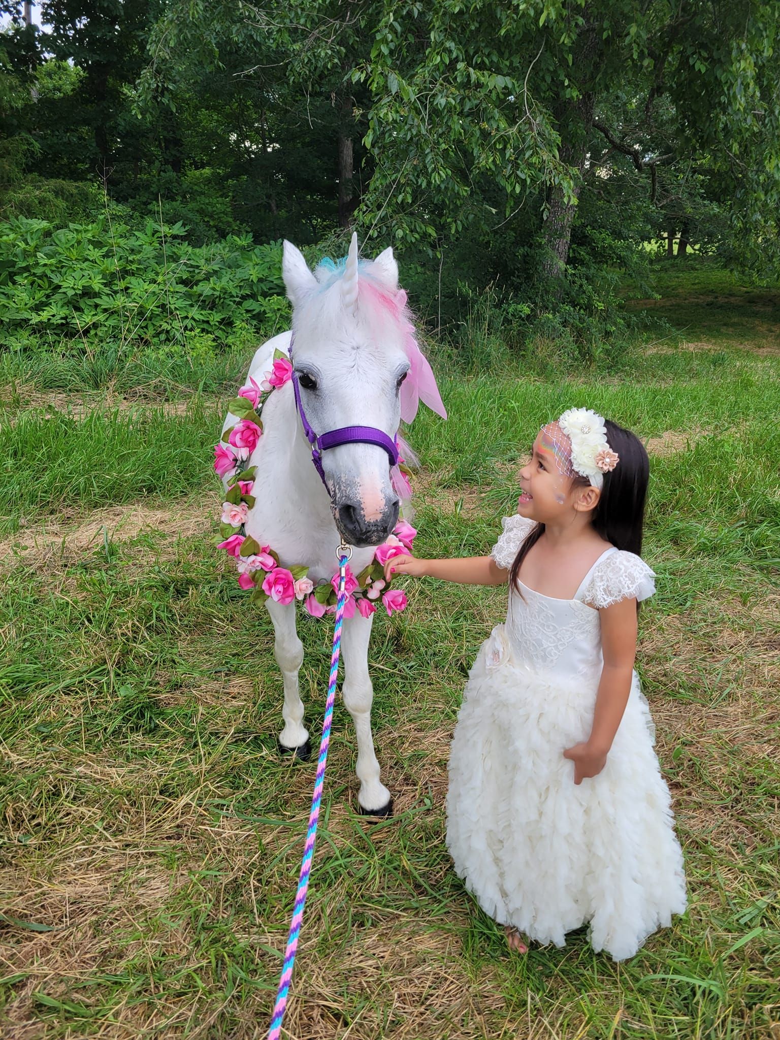 A little girl in a white dress is petting a white unicorn.