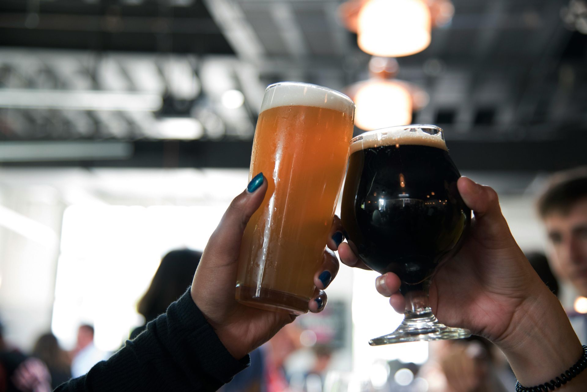 Two hands toasting with glasses of beer, one light, one dark. Bar setting.