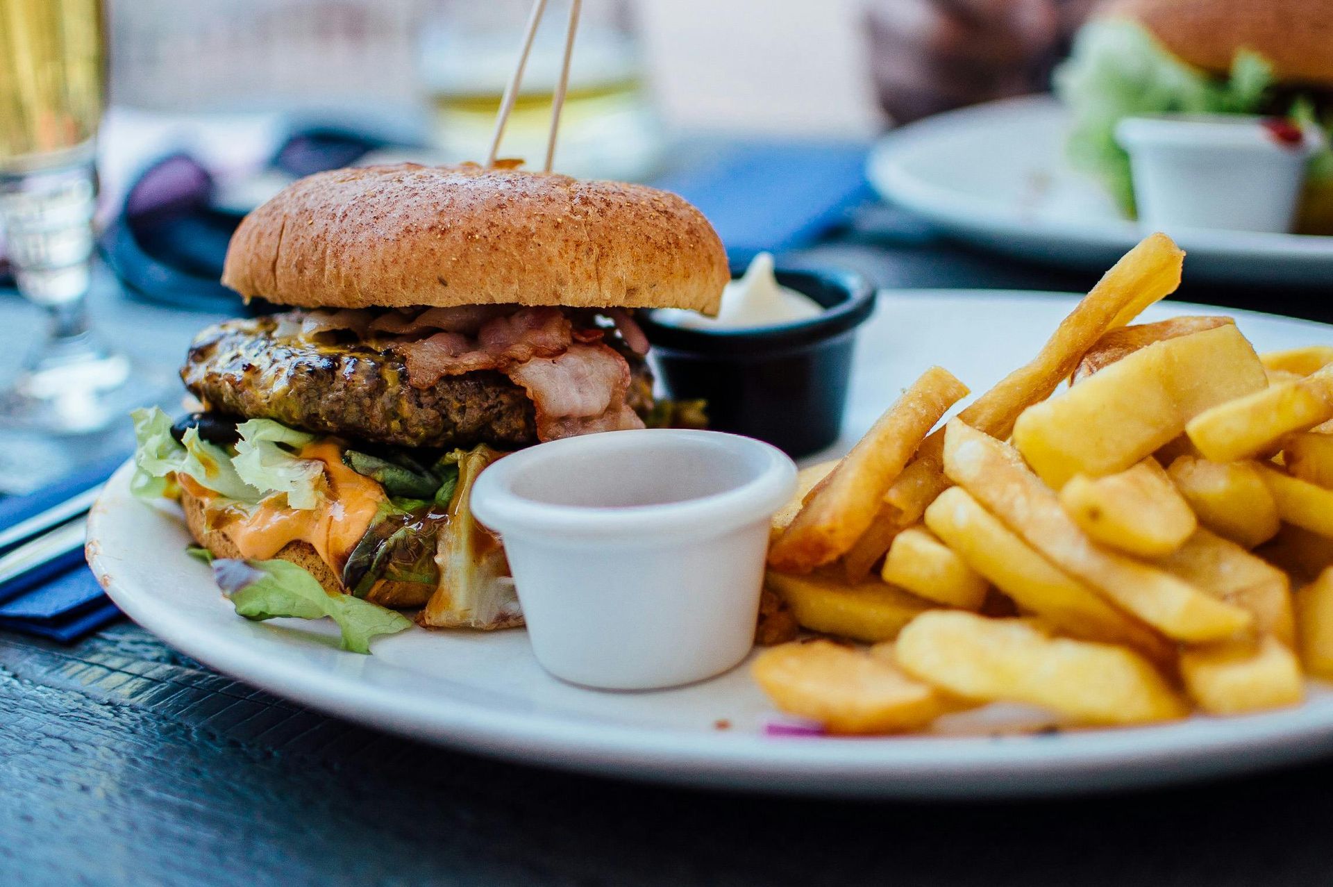 Burger with bacon, lettuce, fries, and dipping sauces on a white plate.