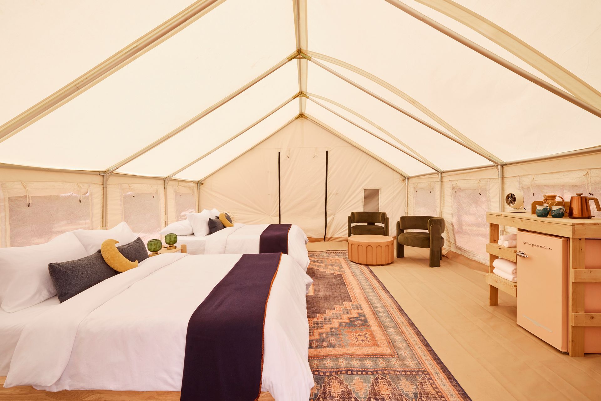 Glamping tent interior with two beds, seating area, and mini-fridge.