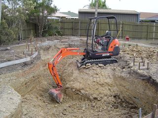 Mini excavator digging in a dirt pit at a construction site. Orange and black machine.