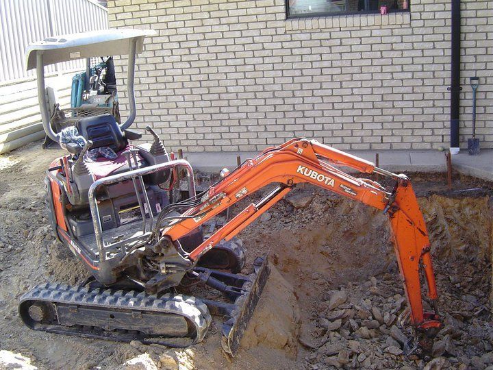 Orange Kubota mini excavator digging in dirt next to a brick building.