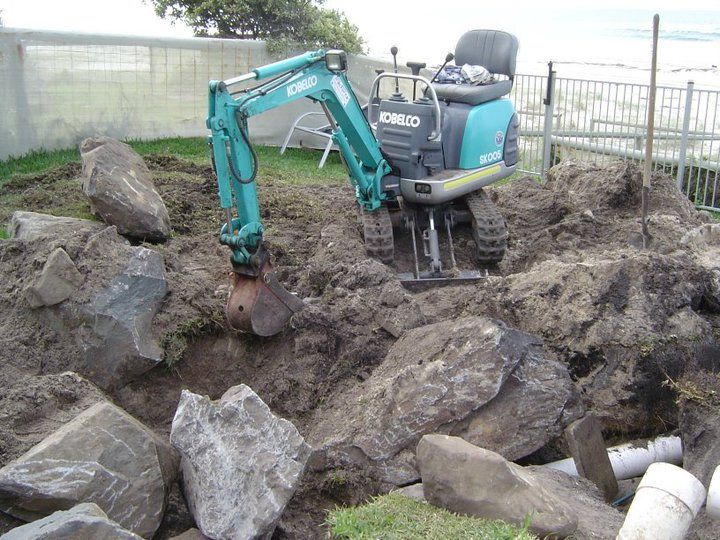 Small teal excavator digging in dirt with rocks.
