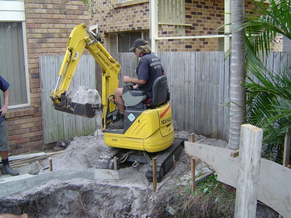 Yellow excavator operator moving a rock in a yard next to a fence.
