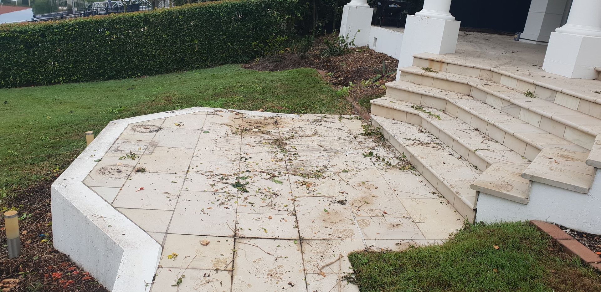 A stone patio and steps leading to a white building; leaves and debris are scattered across the surfaces.