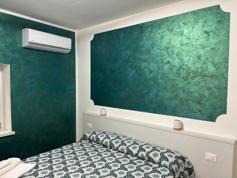 Camera da letto con pareti decorative color verde acqua con texture, letto a fantasia e condizionatore d'aria a parete.