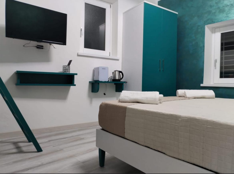 Camera da letto moderna con letto, TV a parete, parete decorativa color verde acqua e piccole mensole.