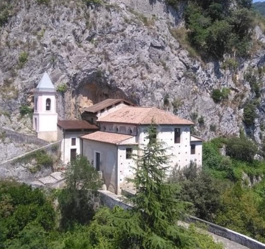 Edifici monastici in pietra con campanile incastonati in una scogliera rocciosa e circondati dal verde.