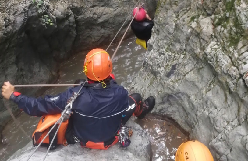 Un alpinista con il casco arancione si cala in corda doppia lungo una fessura rocciosa mentre un'altra persona lo attende più in alto.