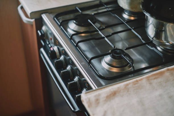 Close-up of a stainless steel stovetop with four burners, knobs, and two pots, with a towel on the side.