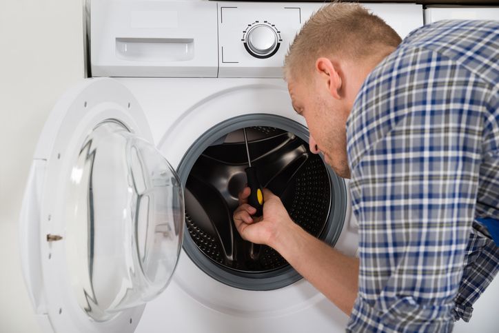 Man using a screwdriver to repair a washing machine.