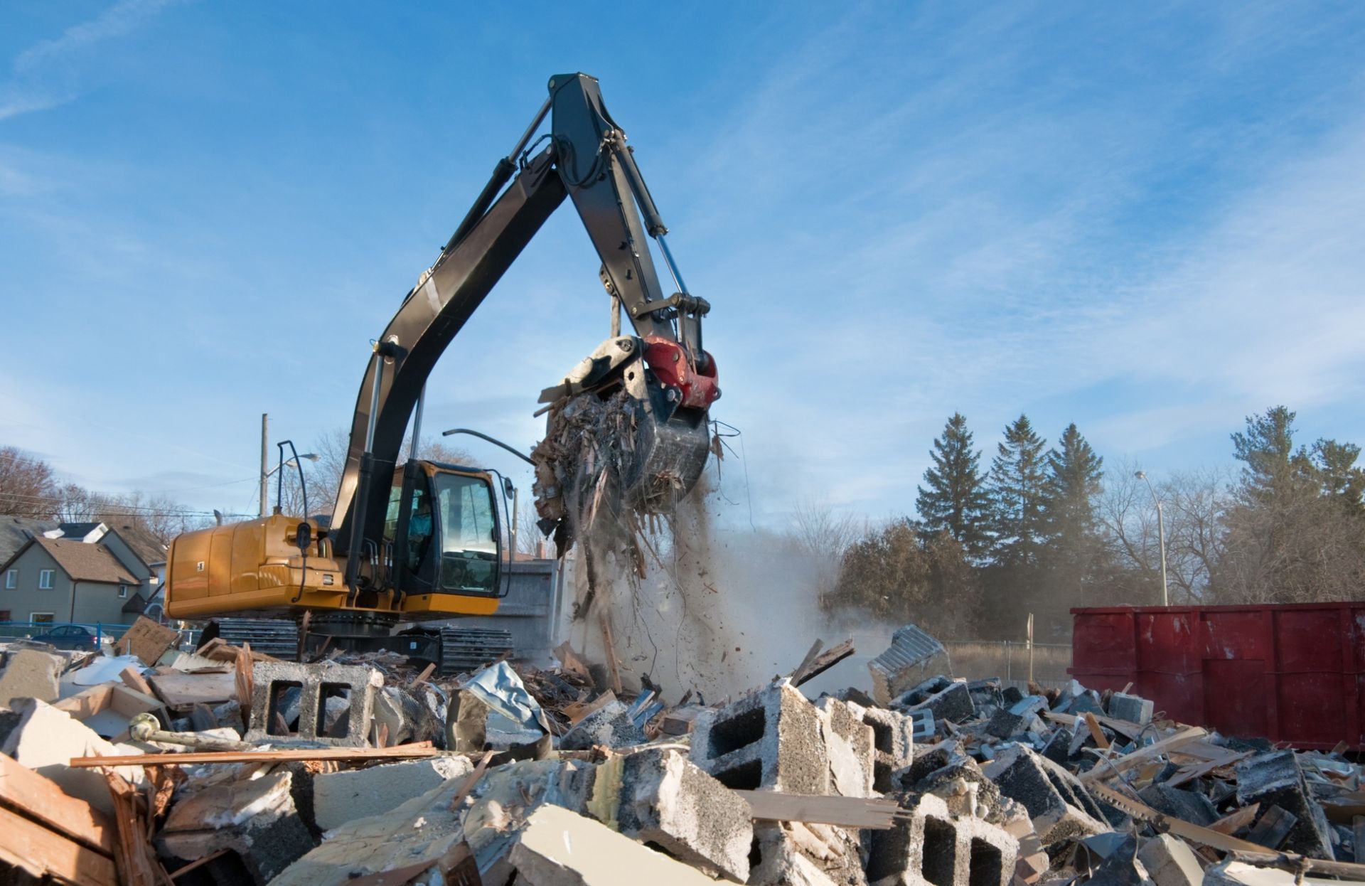 Excavator lifting debris at a demolition site; blue sky, yellow and black machine, rubble.