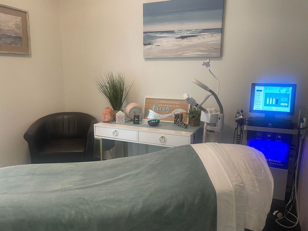 A massage table in a room with a chair and a painting on the wall.