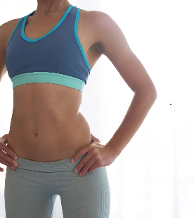 Person in a blue sports bra and gray leggings standing with hands on hips against a white background