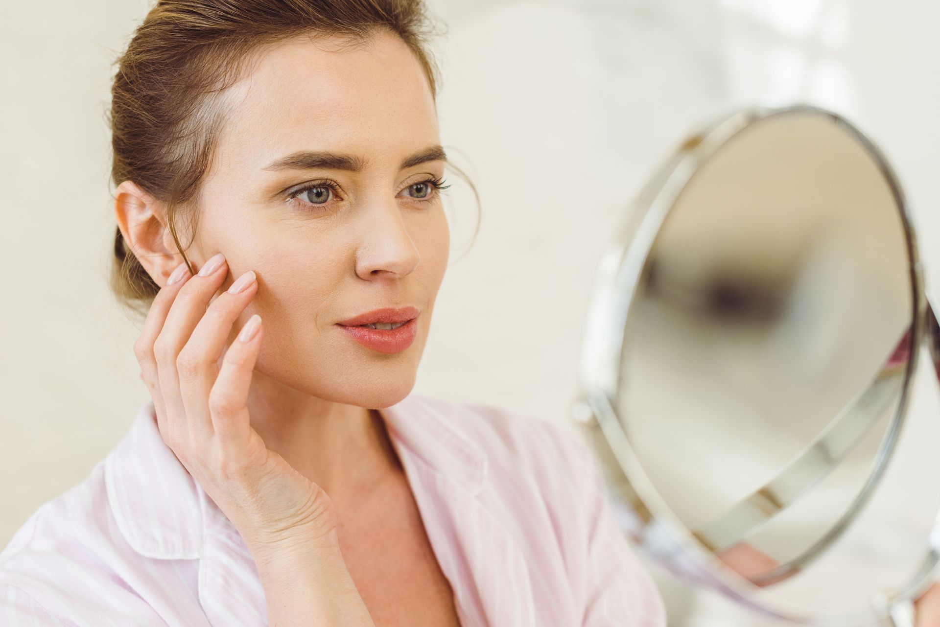 A woman is looking at her face in a mirror.