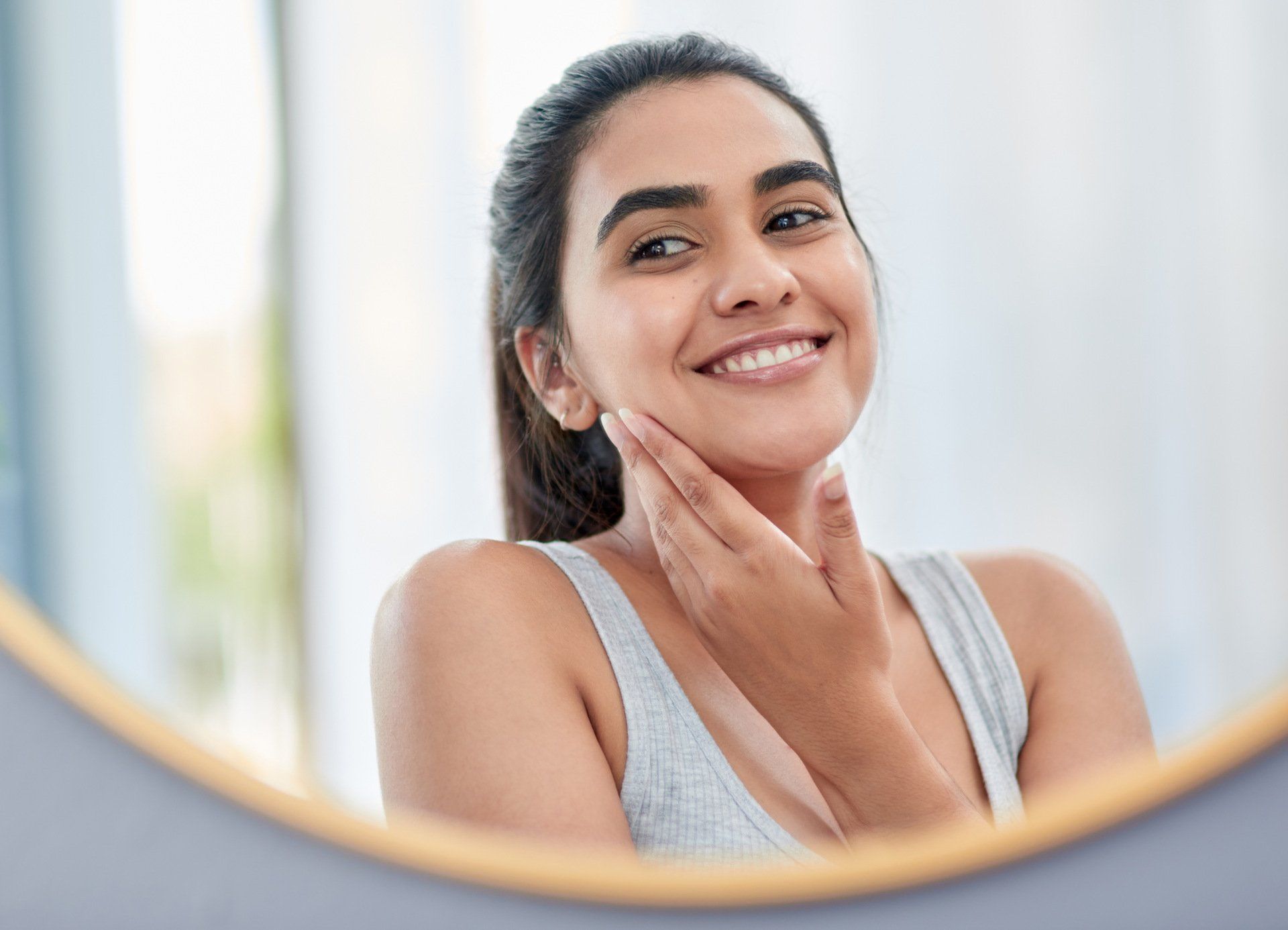 A woman is smiling while looking at her face in a mirror.