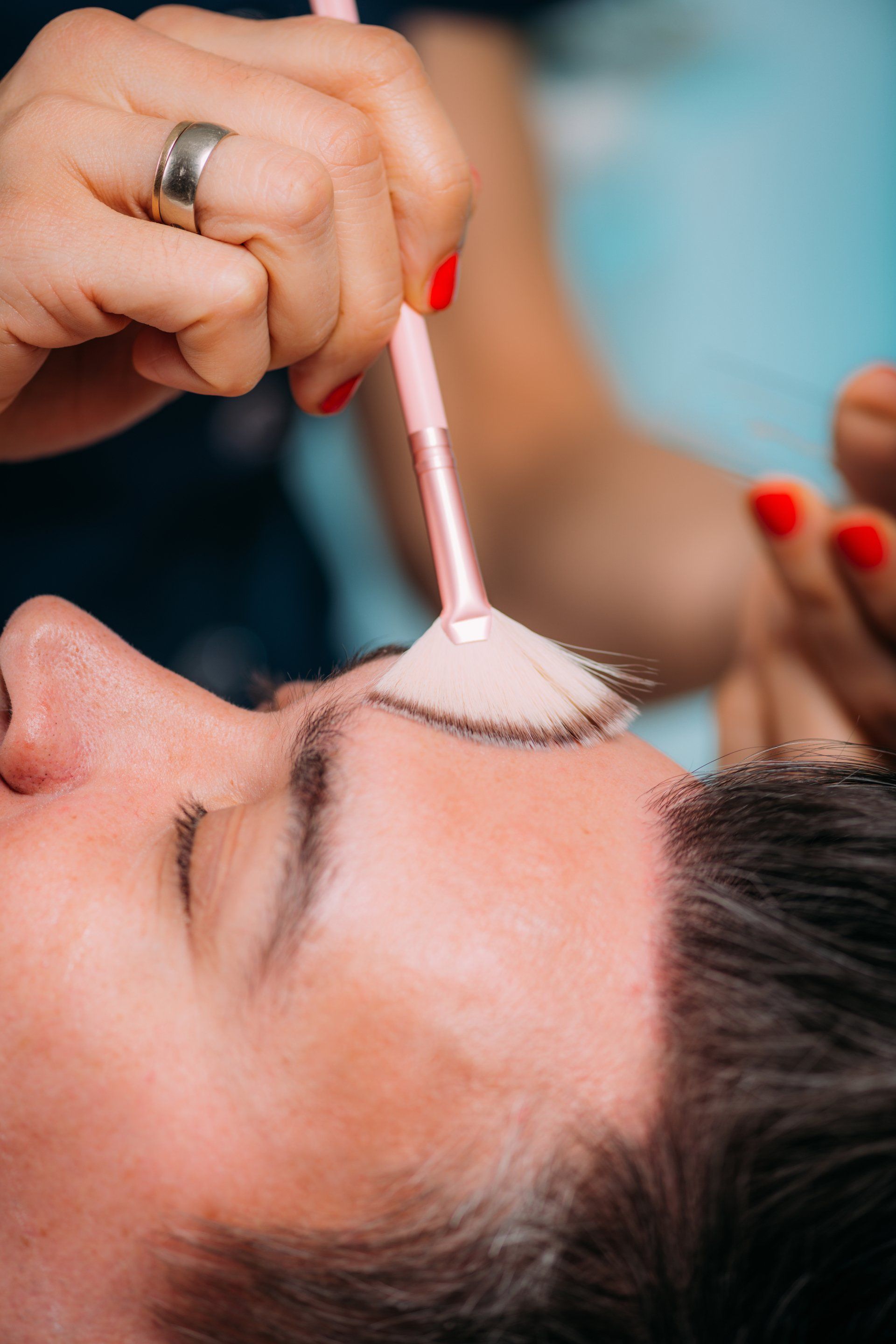 A woman is applying makeup to a man 's face with a brush.