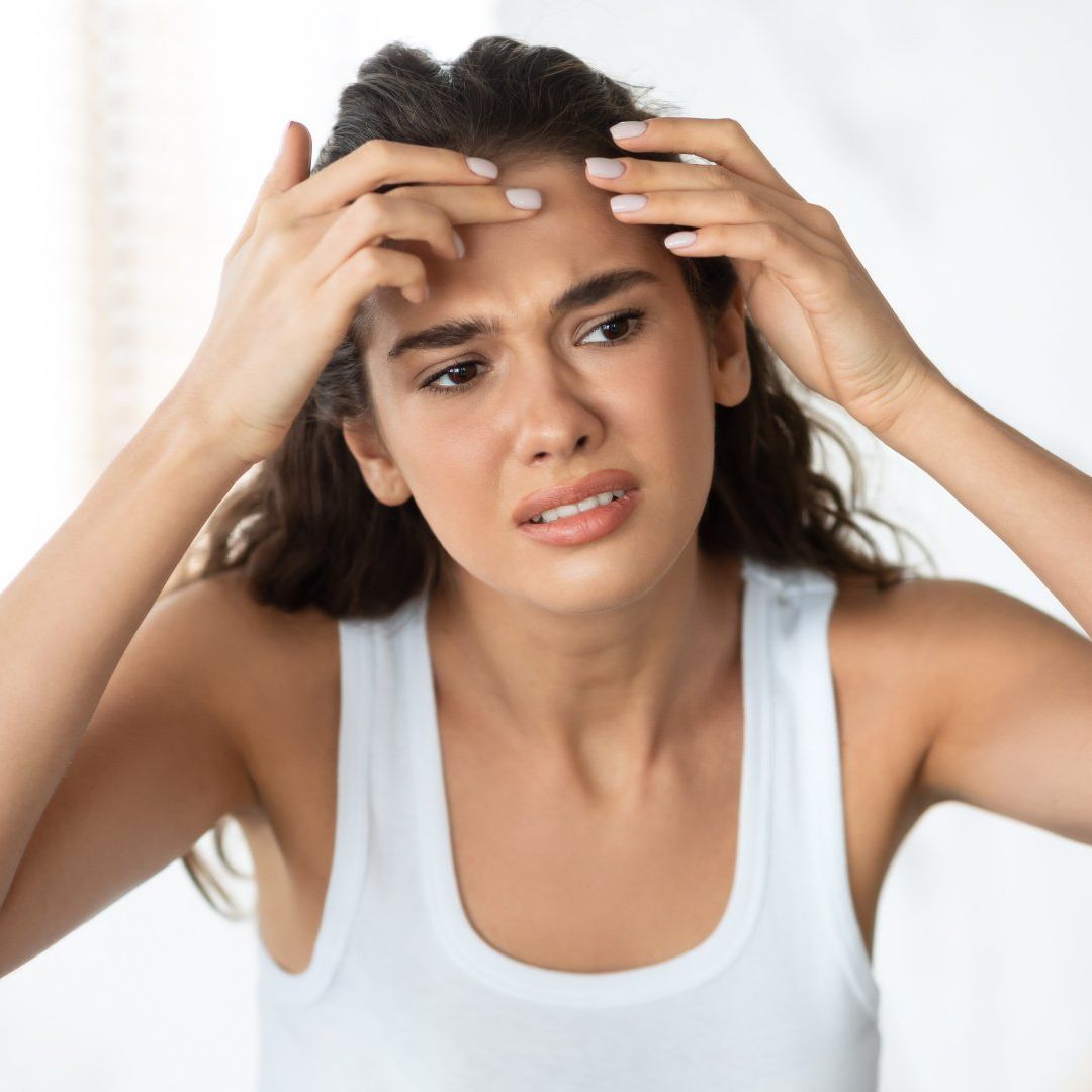 A woman in a white tank top is scratching her forehead