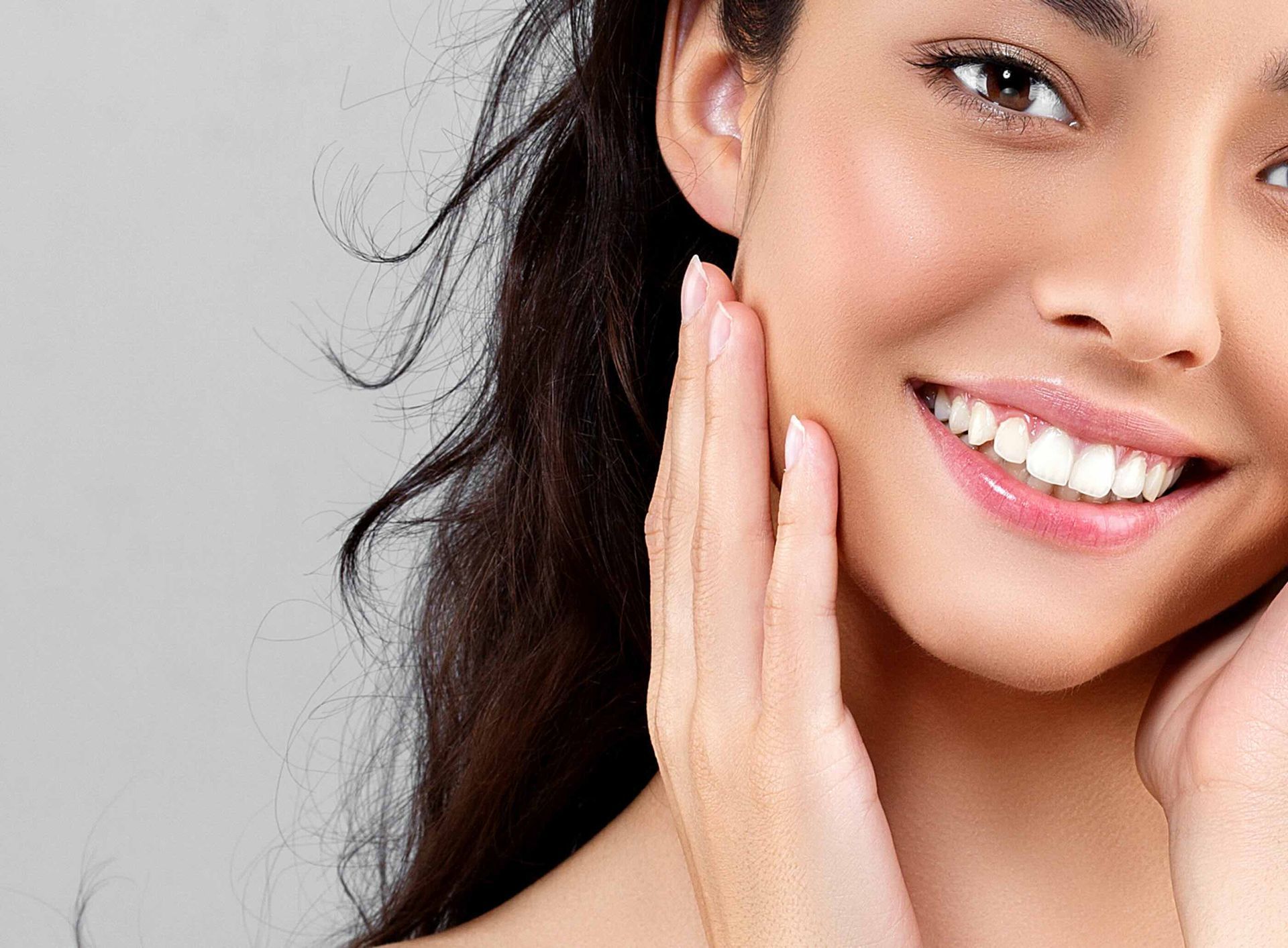 A woman is smiling and touching her face with her hand.