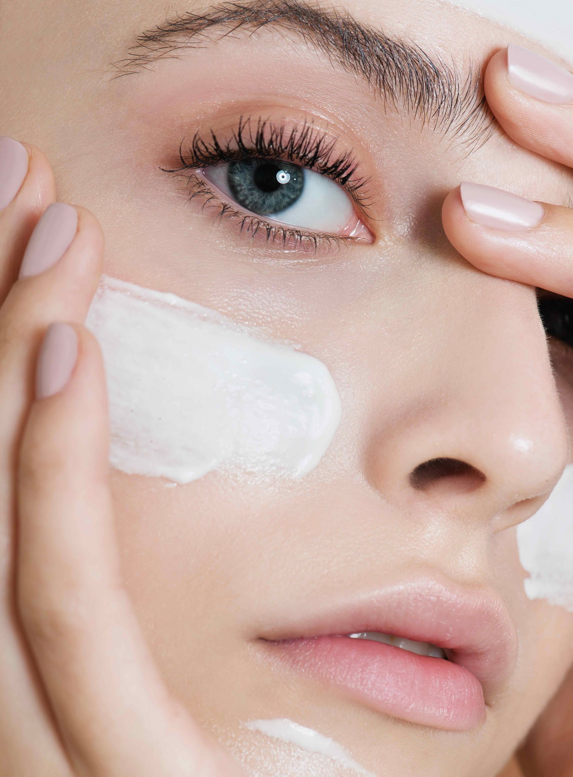 A woman is applying cream to her face.