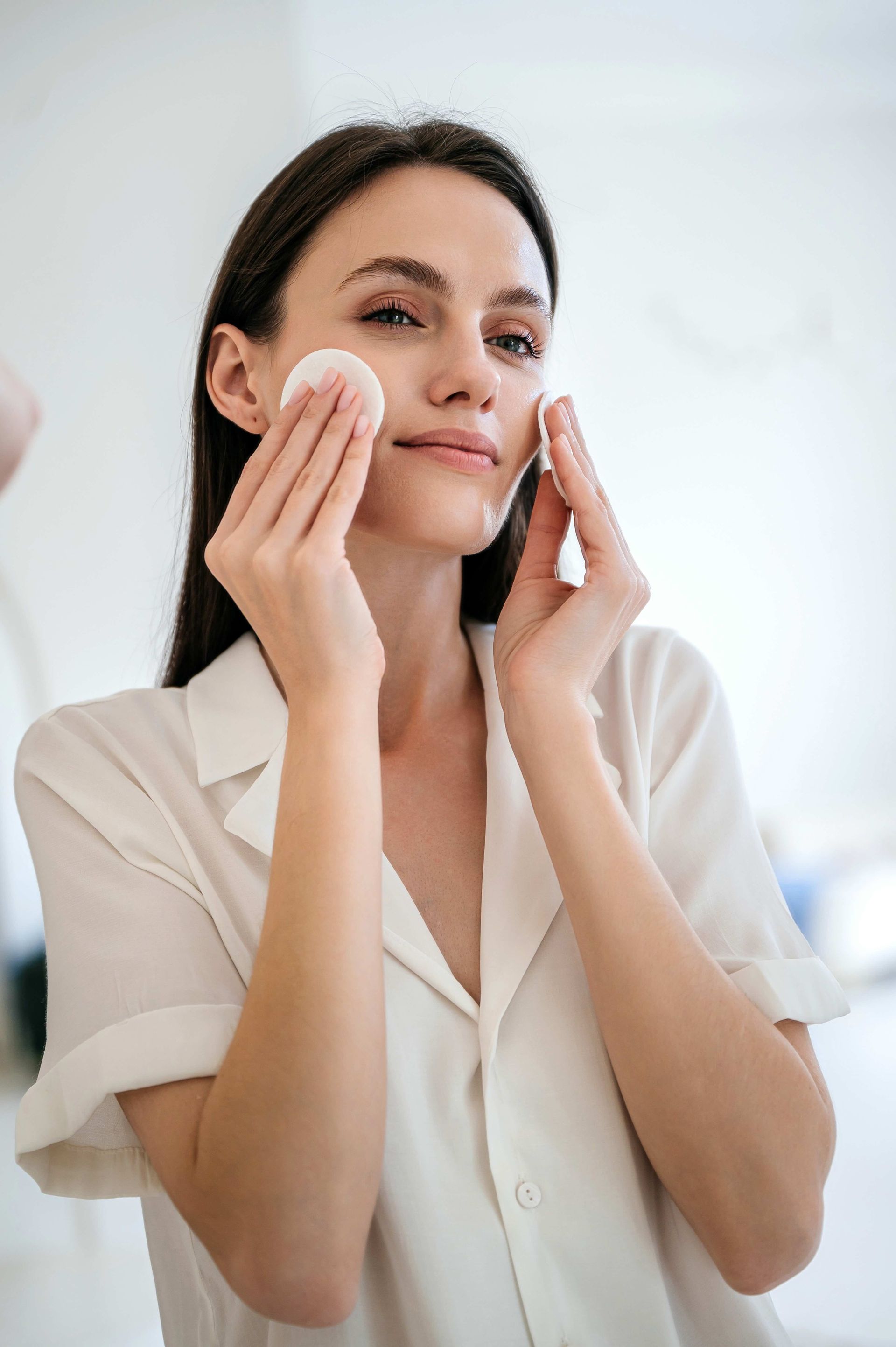 A woman is cleaning her face with cotton swabs in front of a mirror.