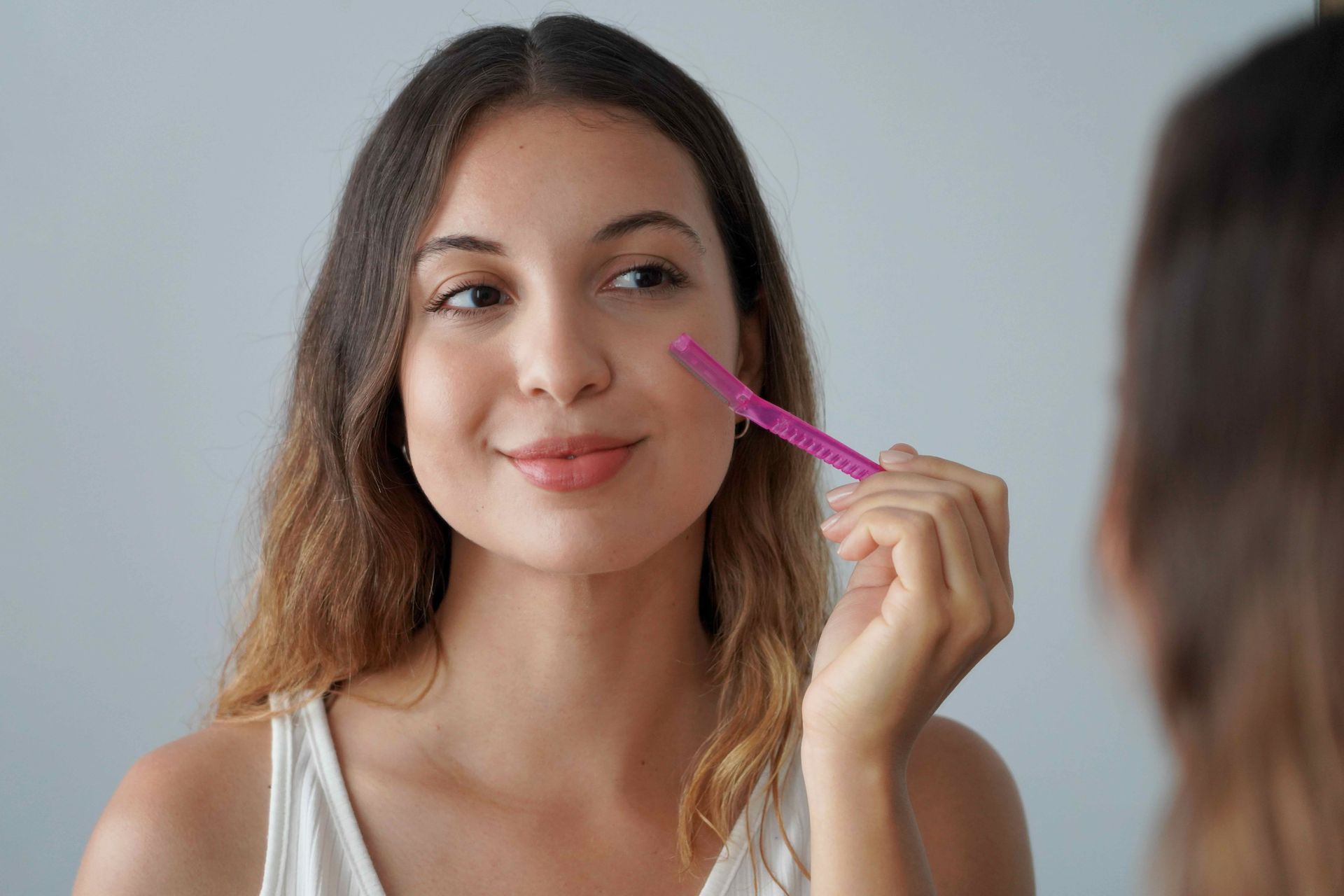 A woman is shaving her face in front of a mirror.