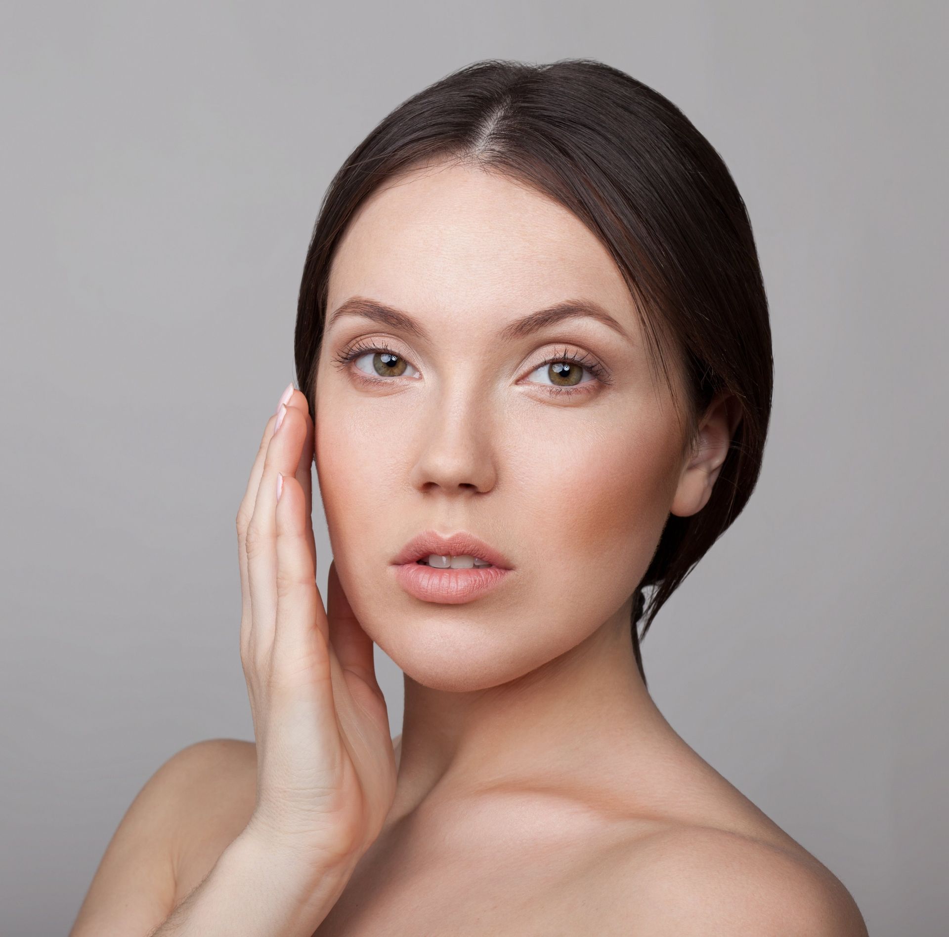 A woman is touching her face with her hand and looking at the camera.