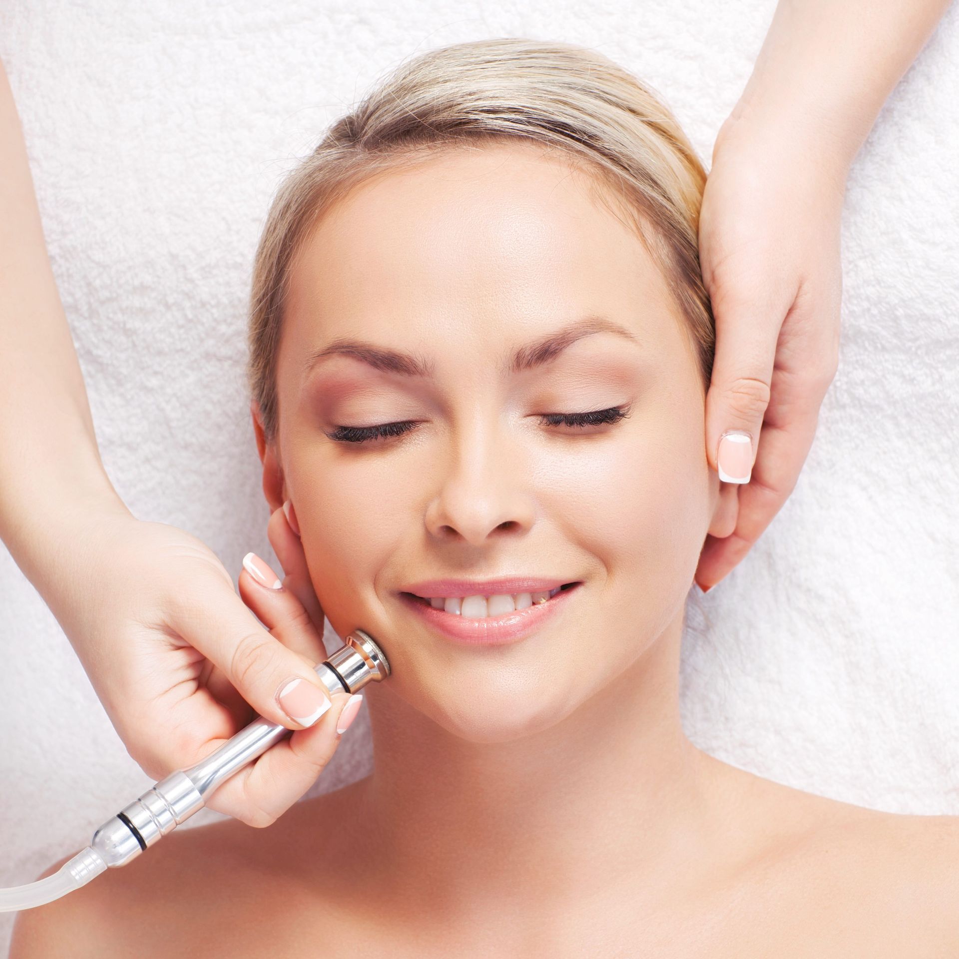 A woman is smiling while getting a treatment on her face