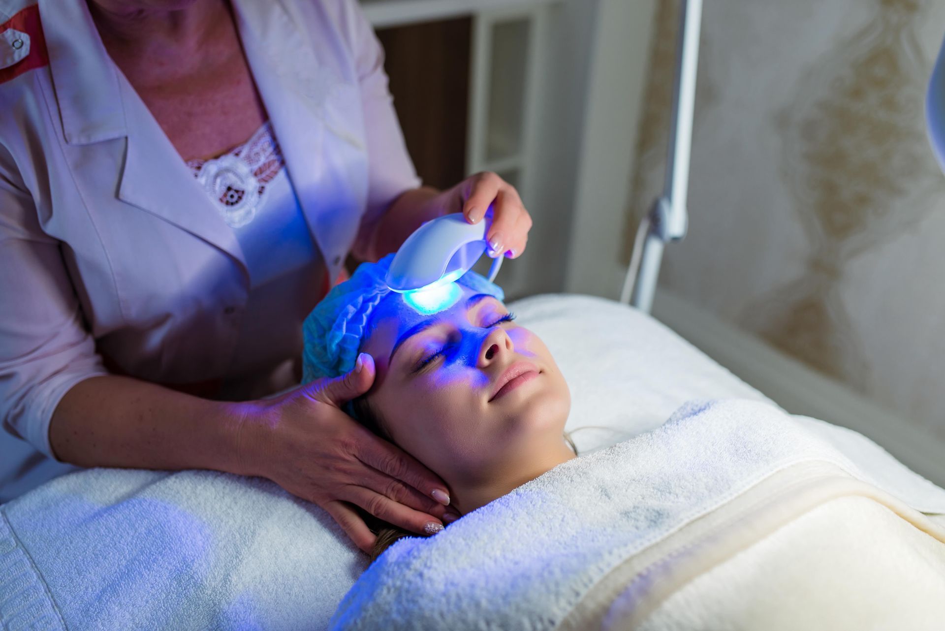 A woman is getting a blue light treatment on her face.