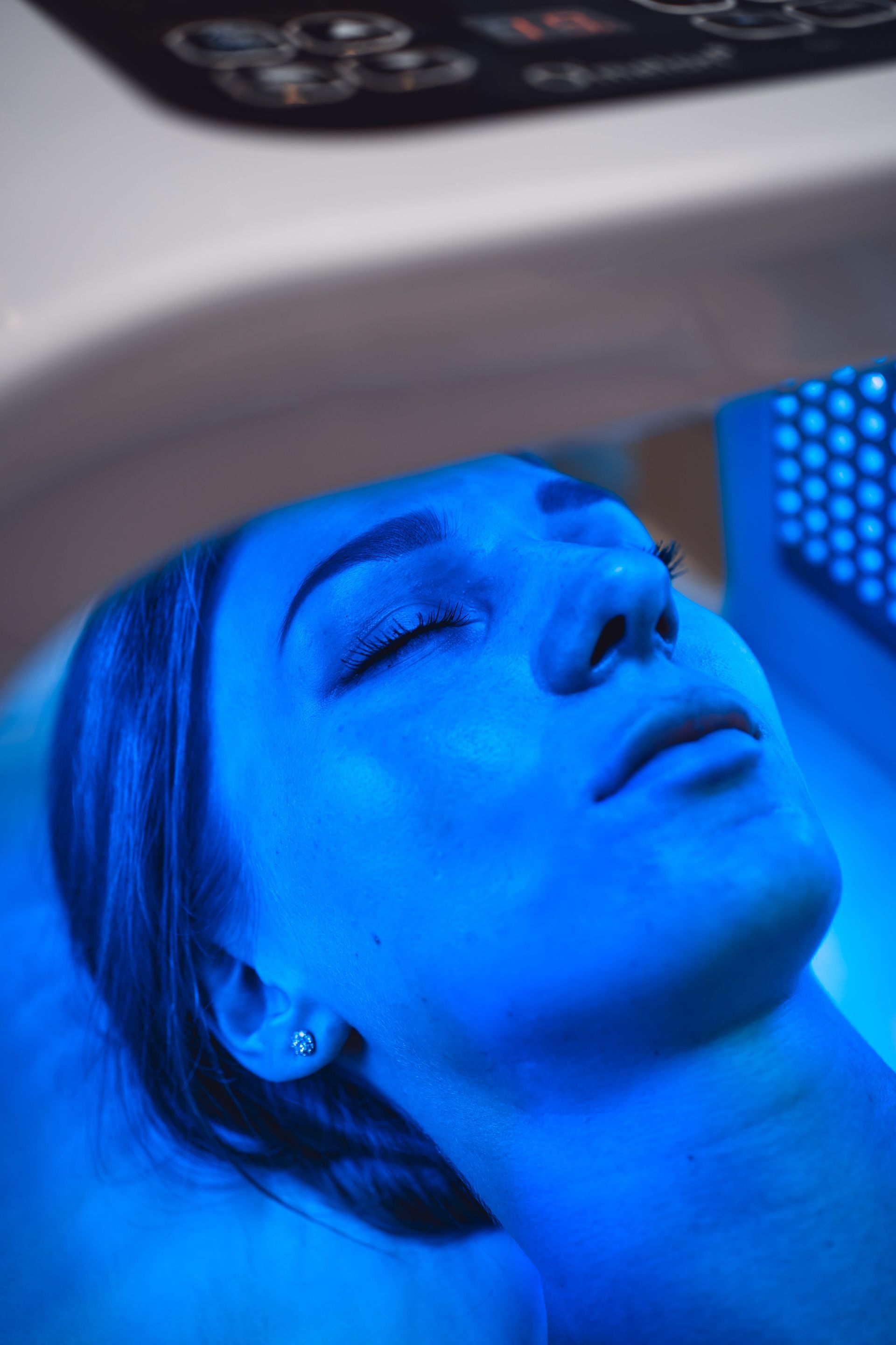 A woman is getting a blue light treatment on her face.