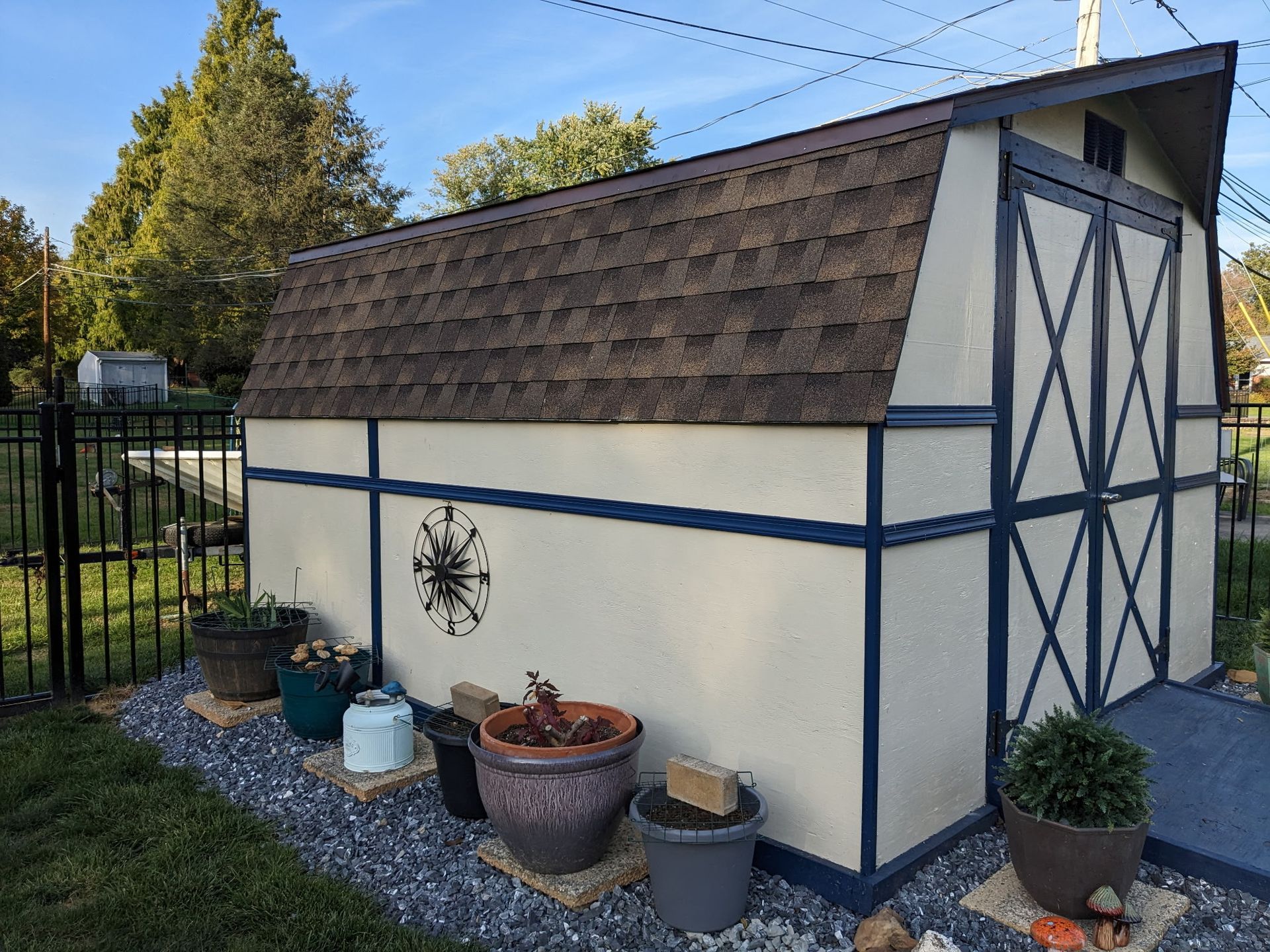 Tan and blue shed with dark brown roof, several potted plants in front.